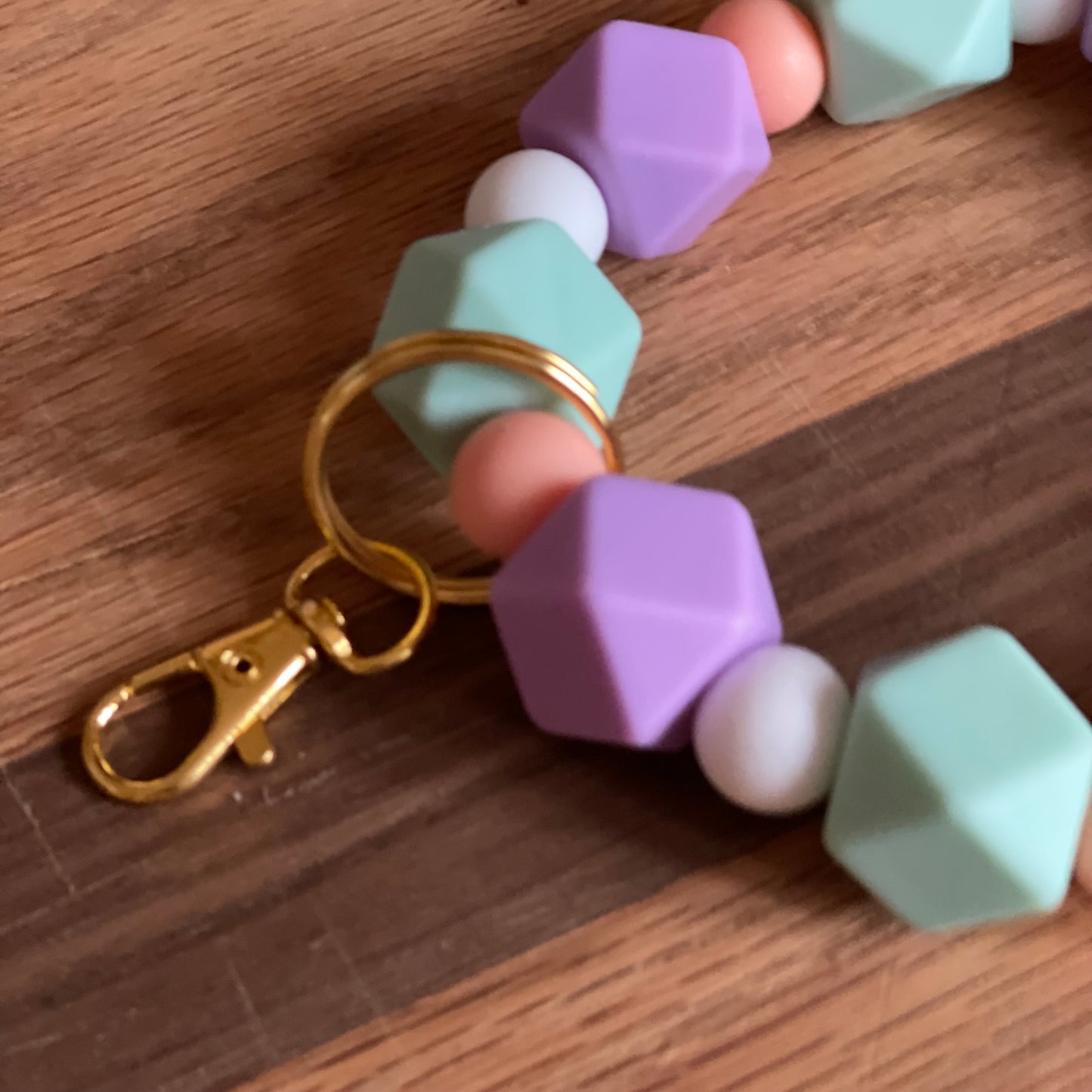 Light purple, peach, turquoise, and white silicone beaded wristlet keychain laying on flat surface focusing on gold keychain attachment