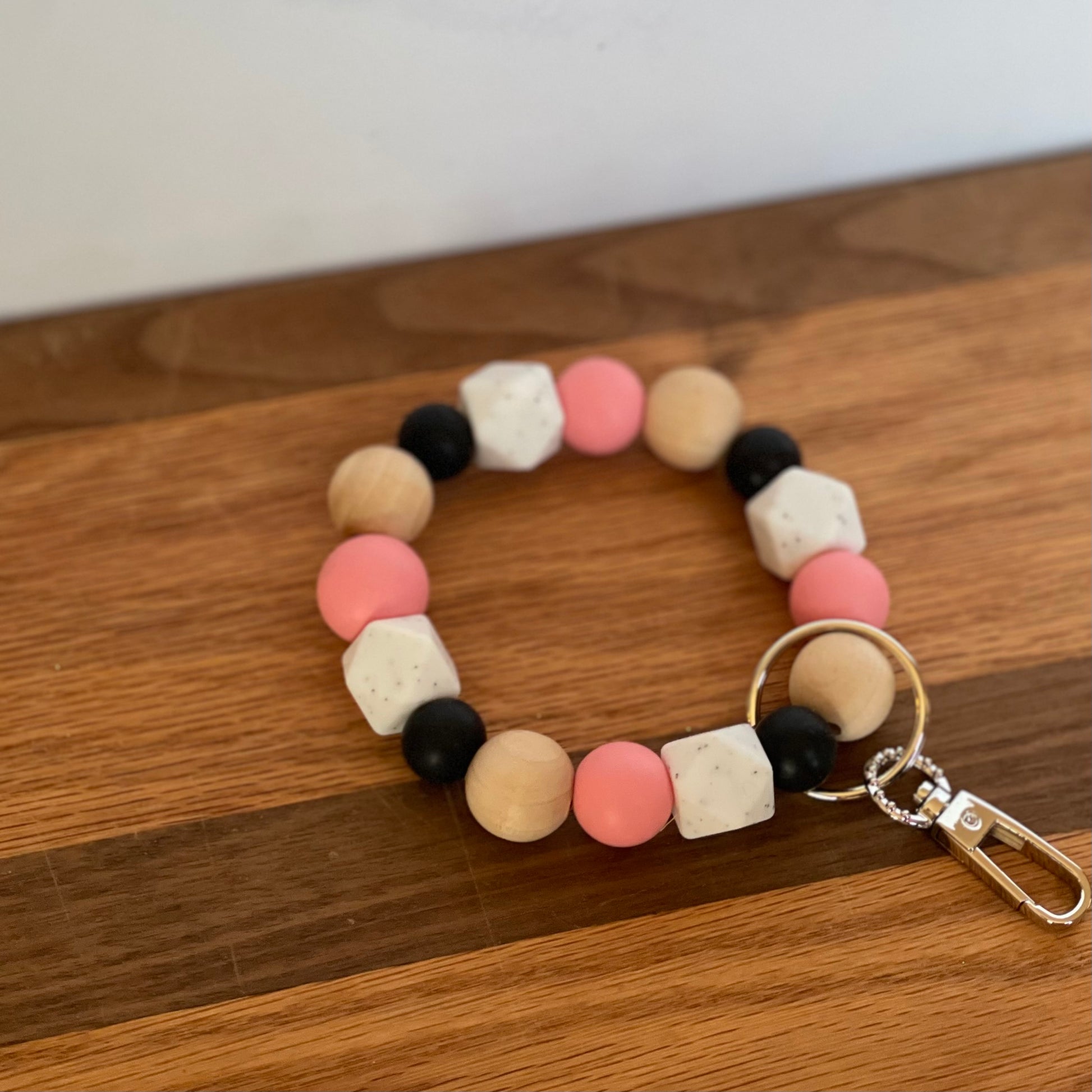 Pink, white, black silicone beads, wood round beads wristlet keychain laying on flat surface