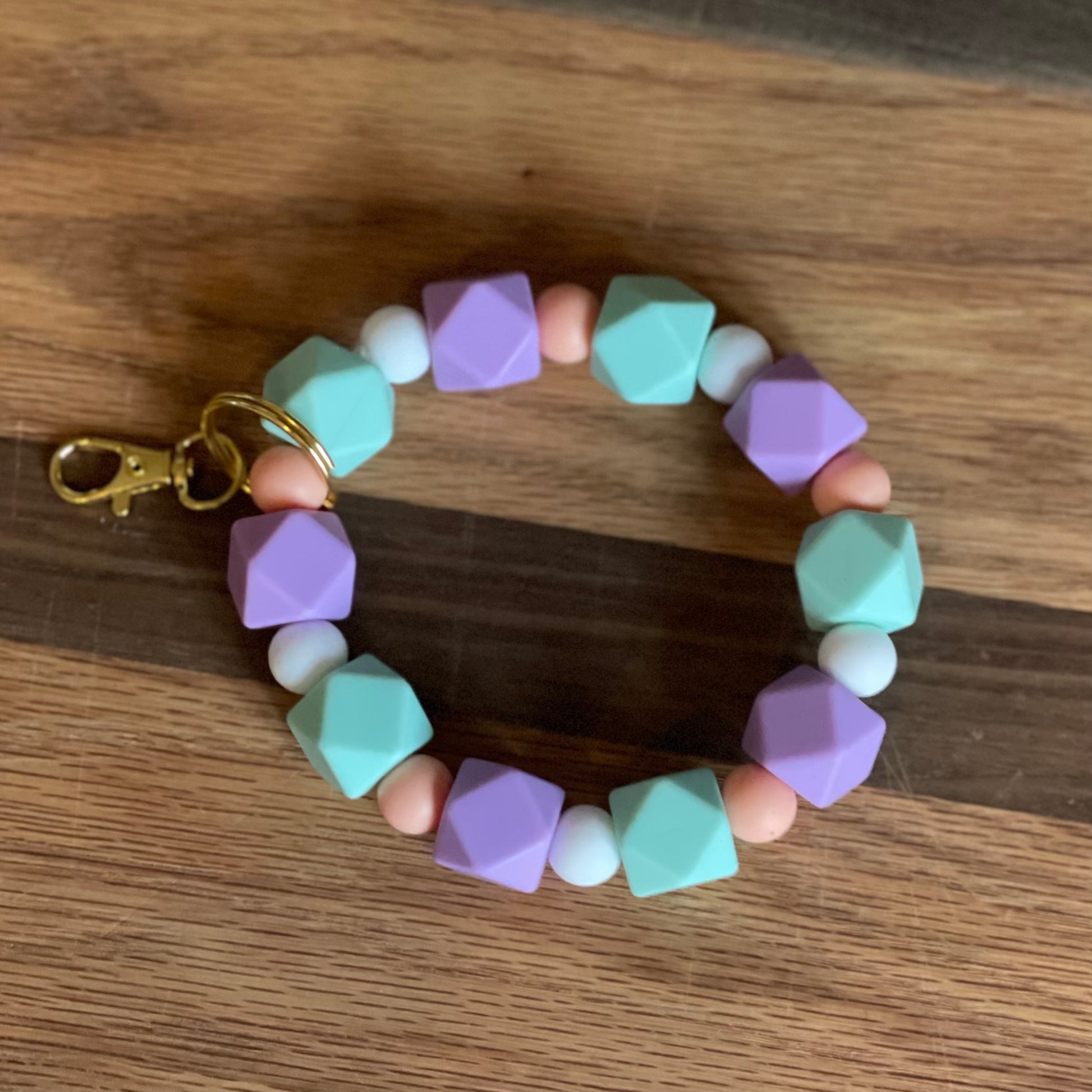 Light purple, peach, turquoise, and white silicone beaded wristlet keychain laying on flat surface