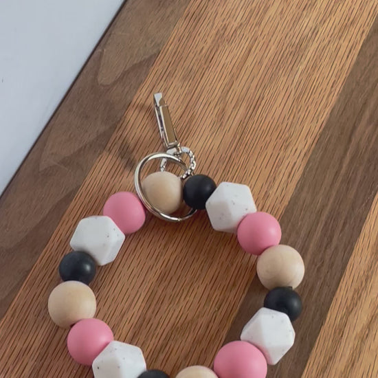Short video of Pink, white, black silicone beads, wood round beads wristlet keychain laying on flat surface