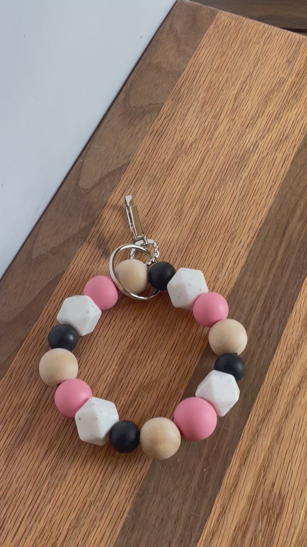 Short video of Pink, white, black silicone beads, wood round beads wristlet keychain laying on flat surface